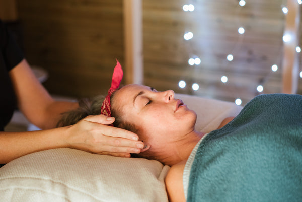 Femme allongée sur une table de massage, elle se fait masser au niveau du visage.