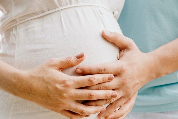 Gros plan sur le ventre d'une femme enceinte, la main de la future maman et celle du futur papa posées dessus