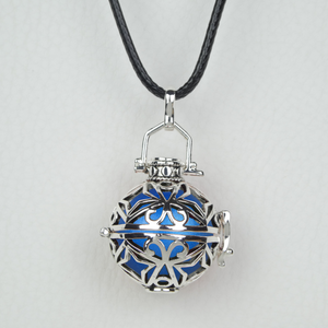 Bola Nusa Dua couleur argent antique présenté suspendu à son cordon ciré noir. Il est constitué d'arabesques et également d'étoiles à 4 branches. Une perle bleue métallisée y est insérée.