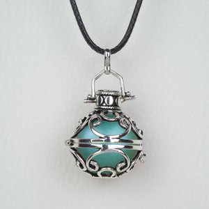 Bola Kuta présenté suspendu à son cordon ciré noir, une perle verte métallisée insérée à l'intérieur. Cette cage de type balinais est faite d'arabesques en argent antique.