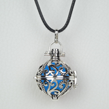 Bola Jimbaran présenté suspendu à son cordon ciré noir. Il s'agit d'une cage faite d'arabesques de couleur argent antique. Une perle bleue y est insérée.