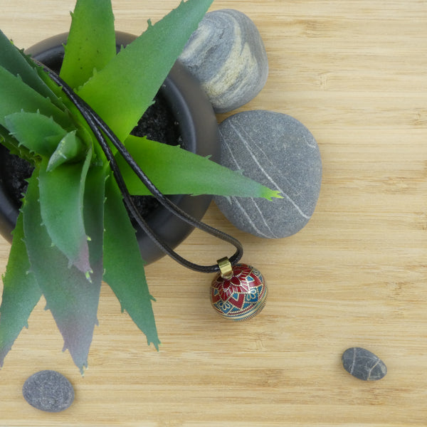 Bola Acapulco bronze présenté dans un décor. Il est déposé sur un support en bois à côté de  cailloux gris à rayures blanches. Une petite plante type cactus est disposée à côté dans un pot noir.