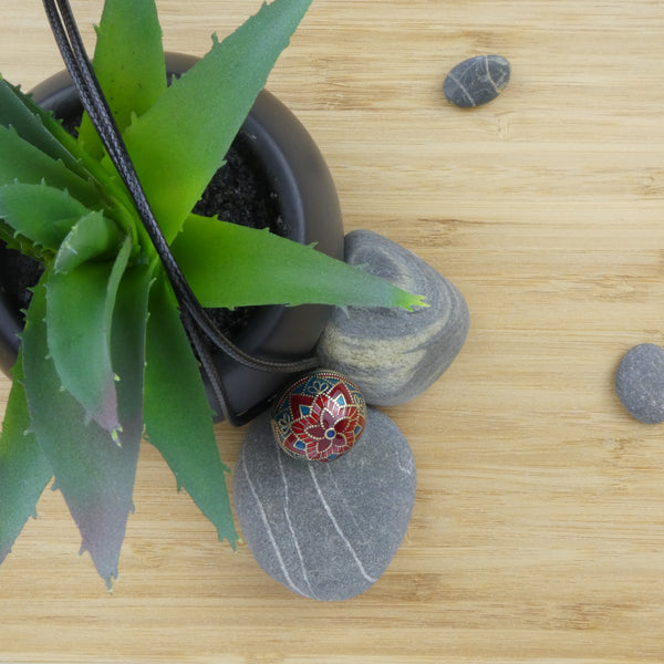 Bola Acapulco argent présenté dans un décor. Il est déposé sur un caillou gris à rayures blanches. Une petite plante type cactus est disposée à côté dans un pot noir. Le tout déposé sur un plateau en bois.