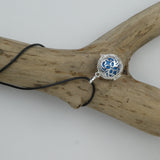 Bola Petites fleurs couleur argent présenté le cordon entouré autour d'une branche de bois sans écorce. La cage renferme une perle bleue métallisée.