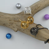 Le Bola Petites fleurs sous ses 3 versions présentés vides sur une branche de bois sans écorce. Bola argent, doré, gun métal. Et au pied de la branche des perles : bleue, violette et anthracite.