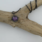 Bola Petites fleurs gun métal présenté le cordon entouré autour d'une branche de bois sans écorce. La cage renferme une perle violette métallisée.