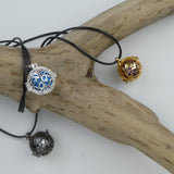 Le Bola Petites fleurs sous ses 3 versions présenté autour d'une branche de bois sans écorce. Bola argent et perle bleue, doré et perle violette et gun métal et perle anthracite.