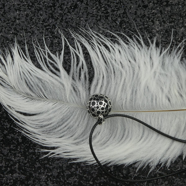 Bola Bubbles dans sa version argentée présenté dans un décor : il est déposé sur une grande plume blanche elle même déposée sur un tissu pailleté noir.