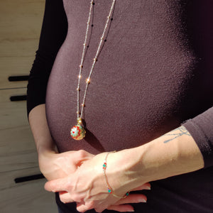 Parure Louisa portée, le pendentif sur le ventre arrondi d'une femme enceinte et le bracelet à son poignet