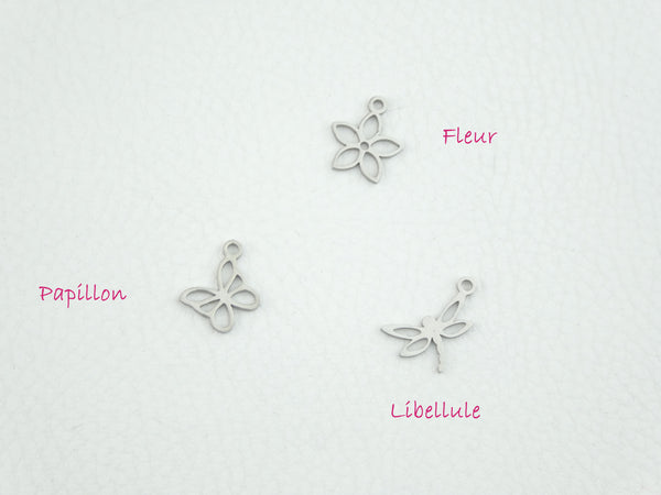 Photo de trois petits pendentifs posés sur un fond blanc : la fleur, la libellule et le papillon.