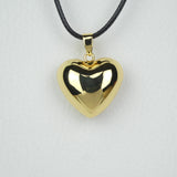 Bola Heart dans sa version or jaune présenté suspendu à son cordon ciré noir. Il s'agit d'un bola de type carillon. Il n'est pas rond, comme les bolas habituels, mais en forme de cœur. 